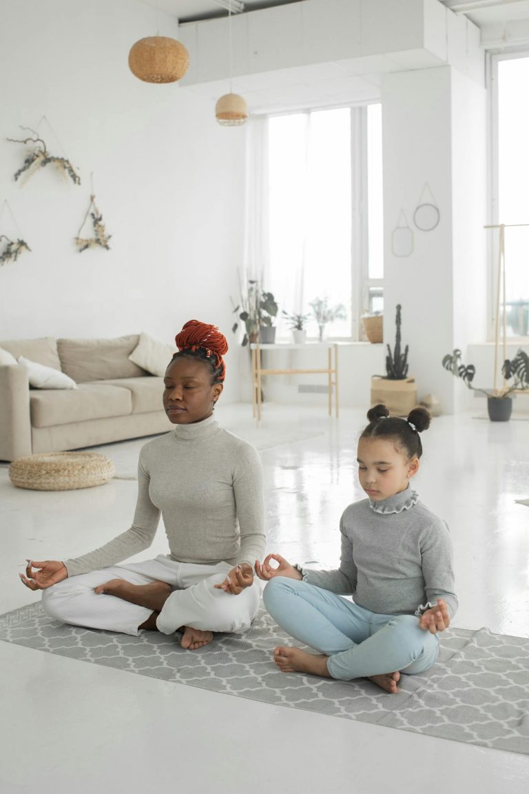 Serene mother and daughter meditating together in a bright living room setting.