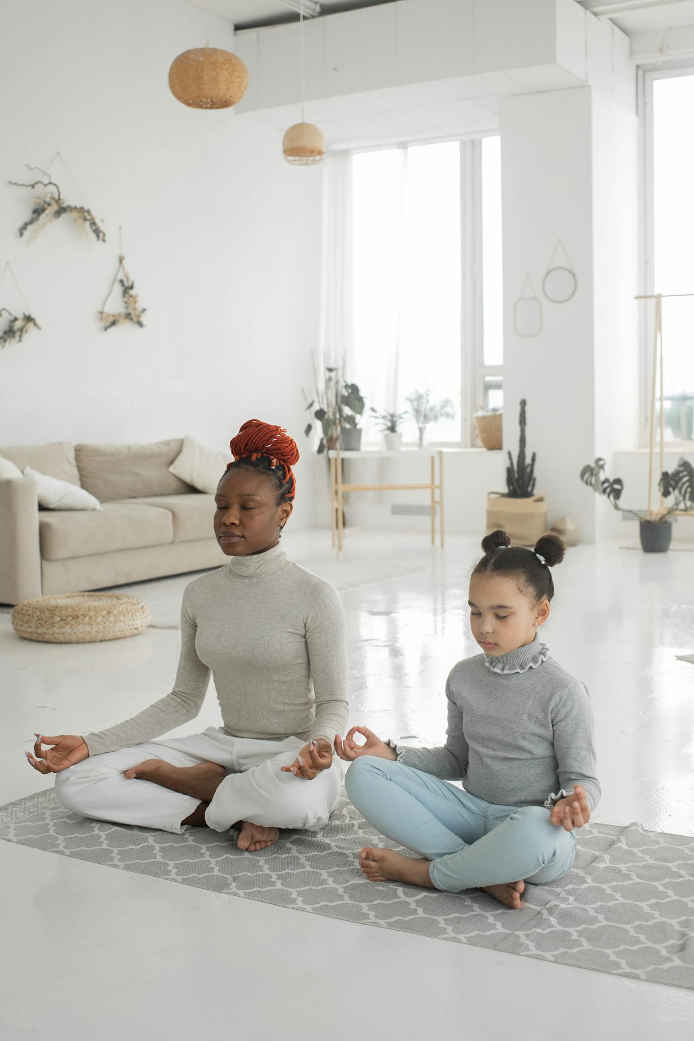 Serene mother and daughter meditating together in a bright living room setting.